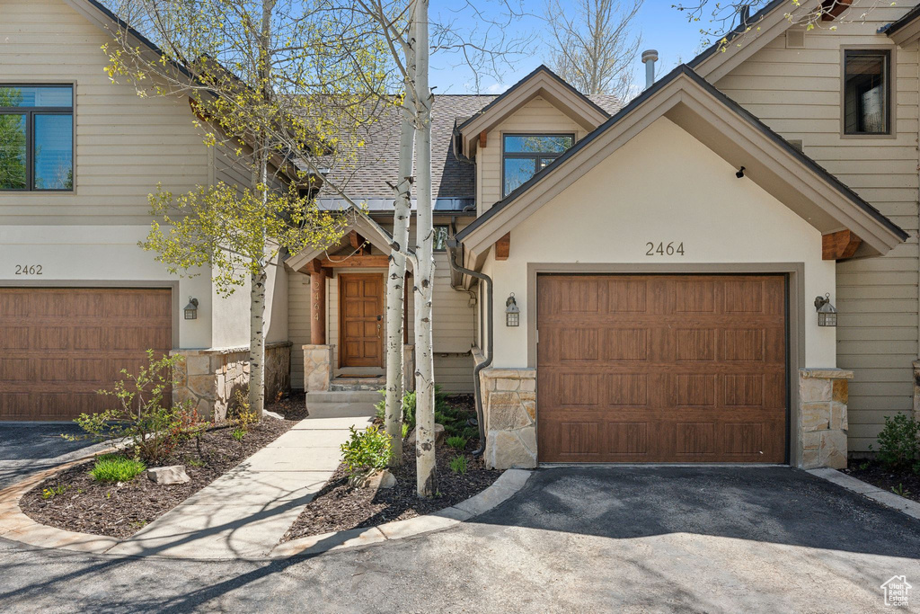 View of front of house with stone siding, driveway, a garage, and roof with shingles
