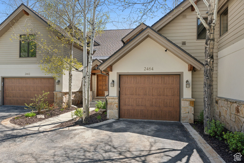 View of front facade with asphalt driveway, stone siding, roof with shingles, stucco siding, and an attached garage