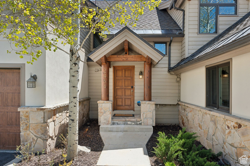 Doorway to property with stone siding and roof with shingles