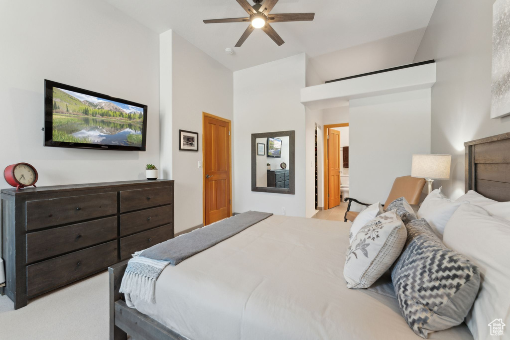 Bedroom with high vaulted ceiling, carpet flooring, ceiling fan, and connected bathroom
