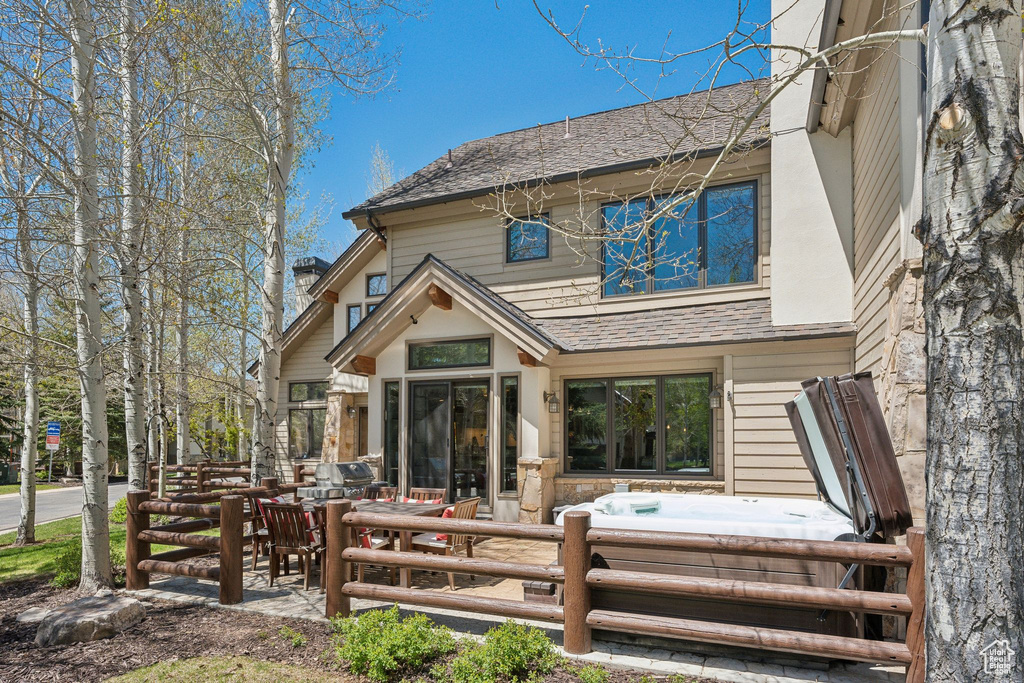 Back of property with a hot tub and roof with shingles