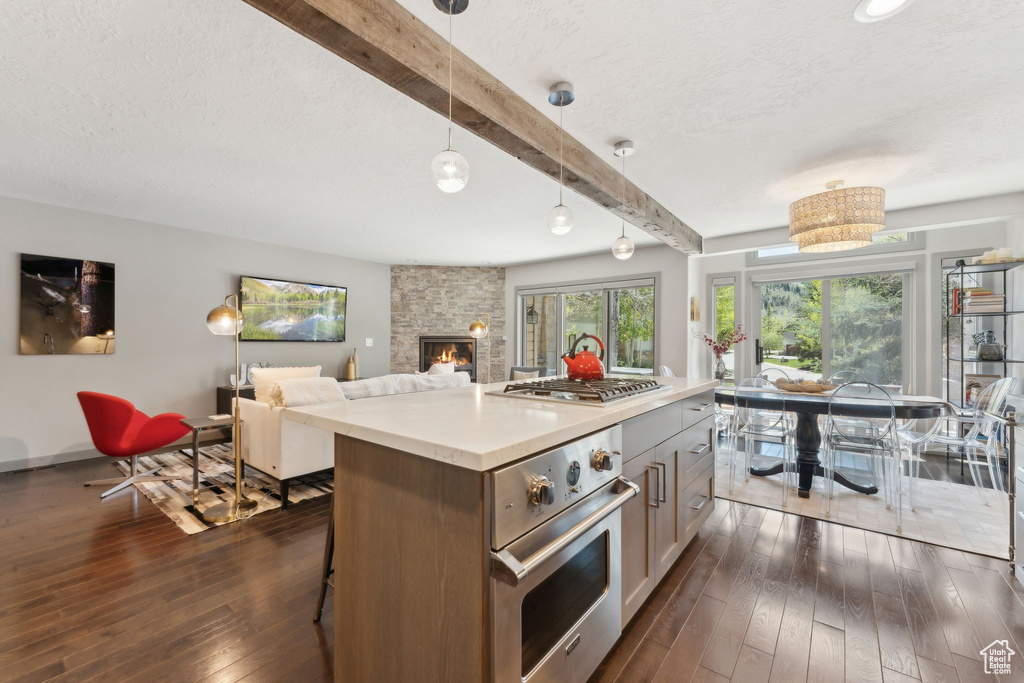 Kitchen with appliances with stainless steel finishes, beam ceiling, dark wood finished floors, a textured ceiling, and a fireplace