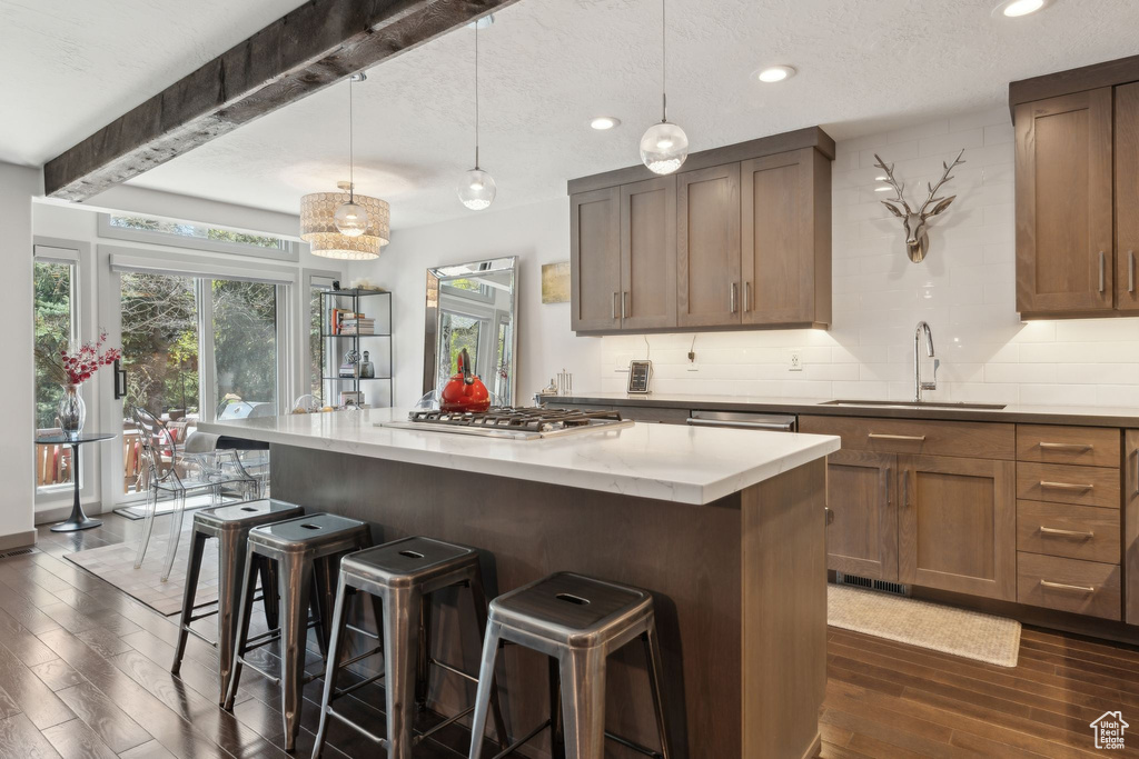Kitchen featuring a sink, stainless steel gas cooktop, dark wood finished floors, beamed ceiling, and a breakfast bar