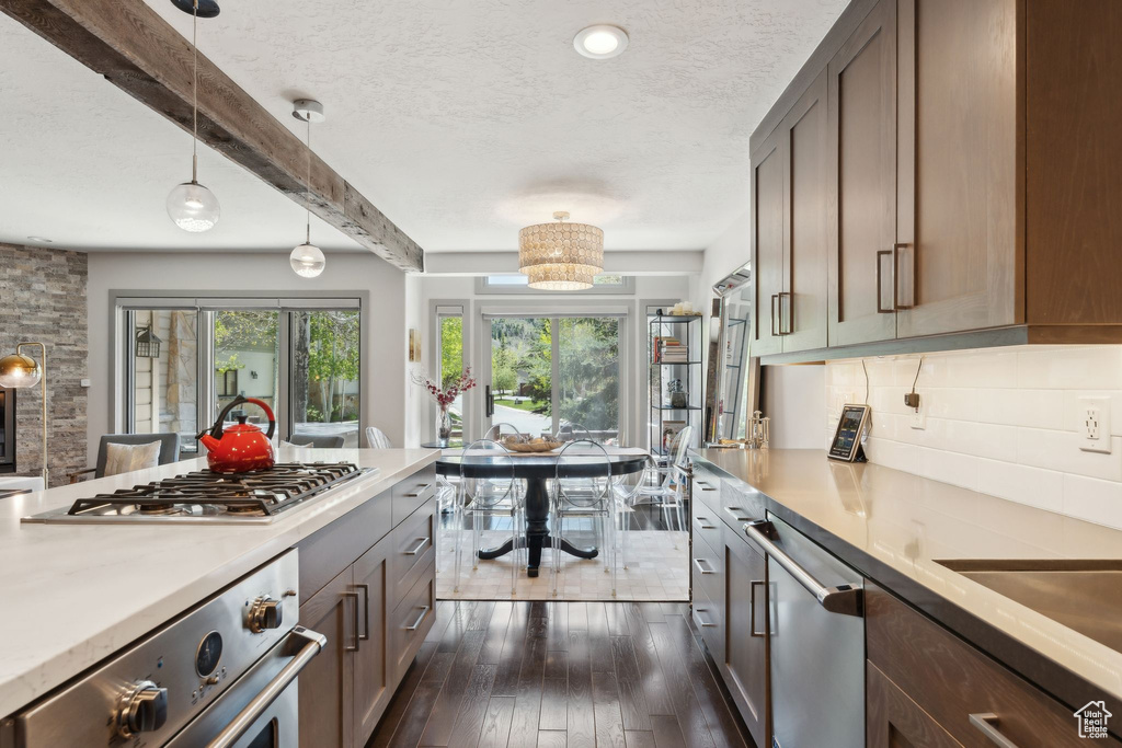 Kitchen with stainless steel appliances, light countertops, a textured ceiling, decorative backsplash, and dark wood finished floors