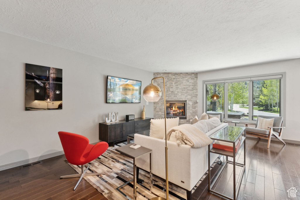 Living area with wood-type flooring, a textured ceiling, a stone fireplace, and baseboards