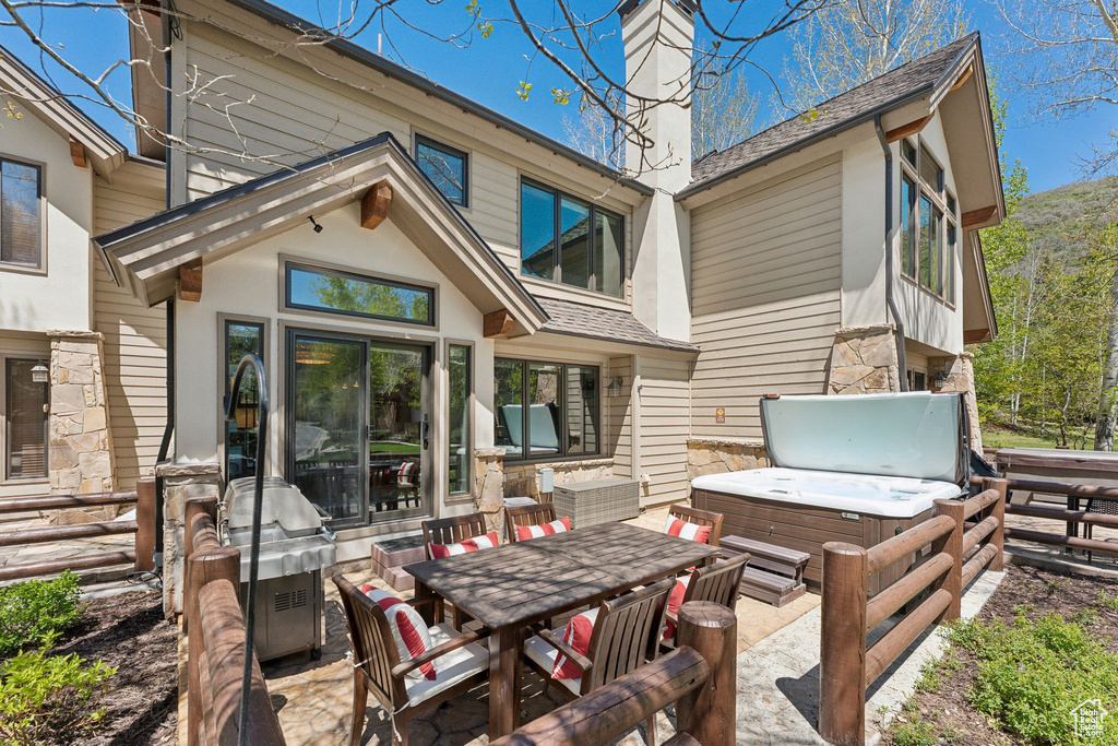Rear view of property featuring a hot tub, a chimney, roof with shingles, a patio area, and stone siding