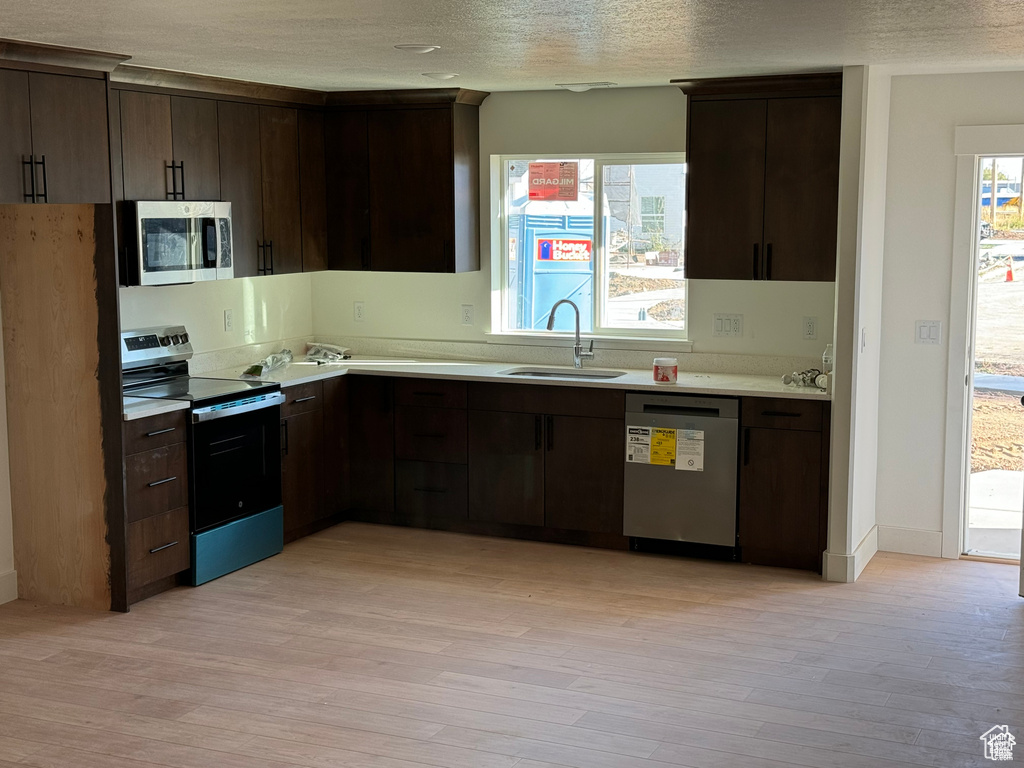 Kitchen featuring stainless steel appliances, a sink, light countertops, dark brown cabinetry, and light wood-style floors