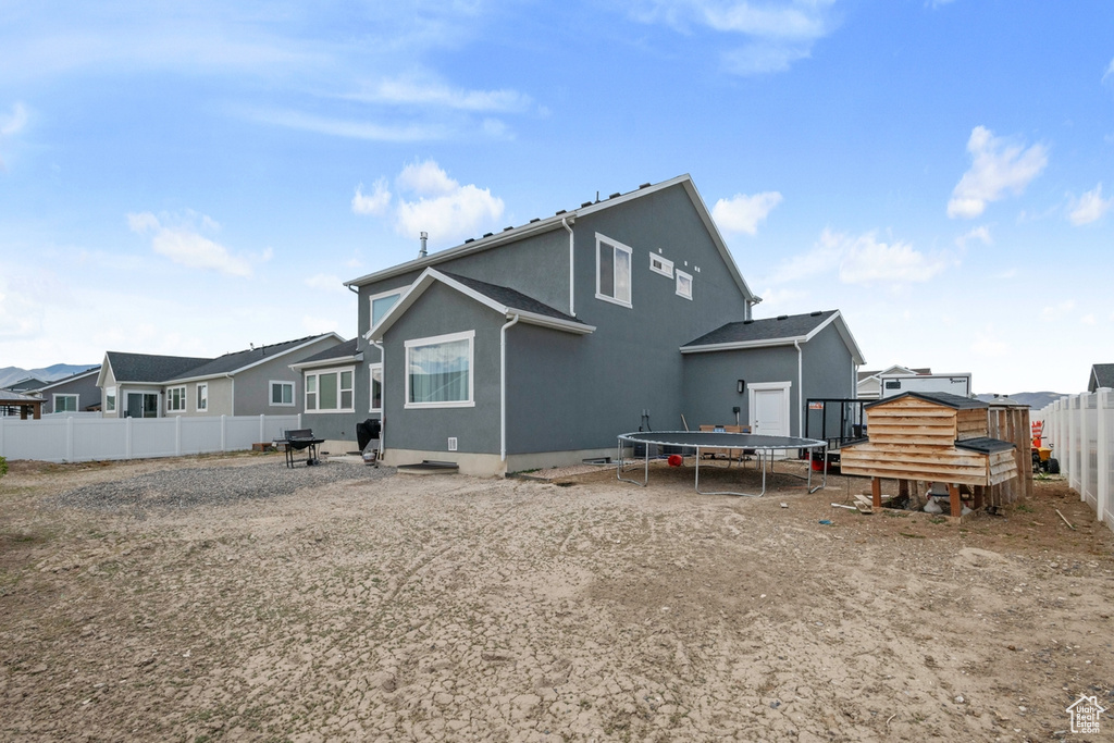 Rear view of house featuring a trampoline, a fenced backyard, and stucco siding