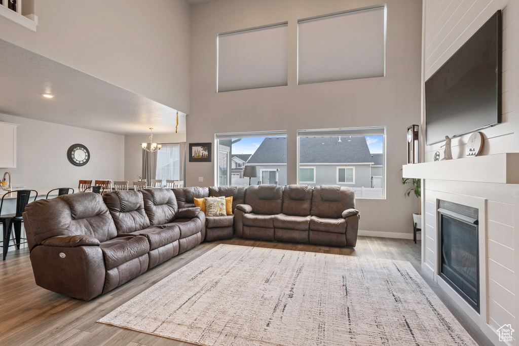 Living room with wood finished floors, a chandelier, a fireplace, a high ceiling, and baseboards