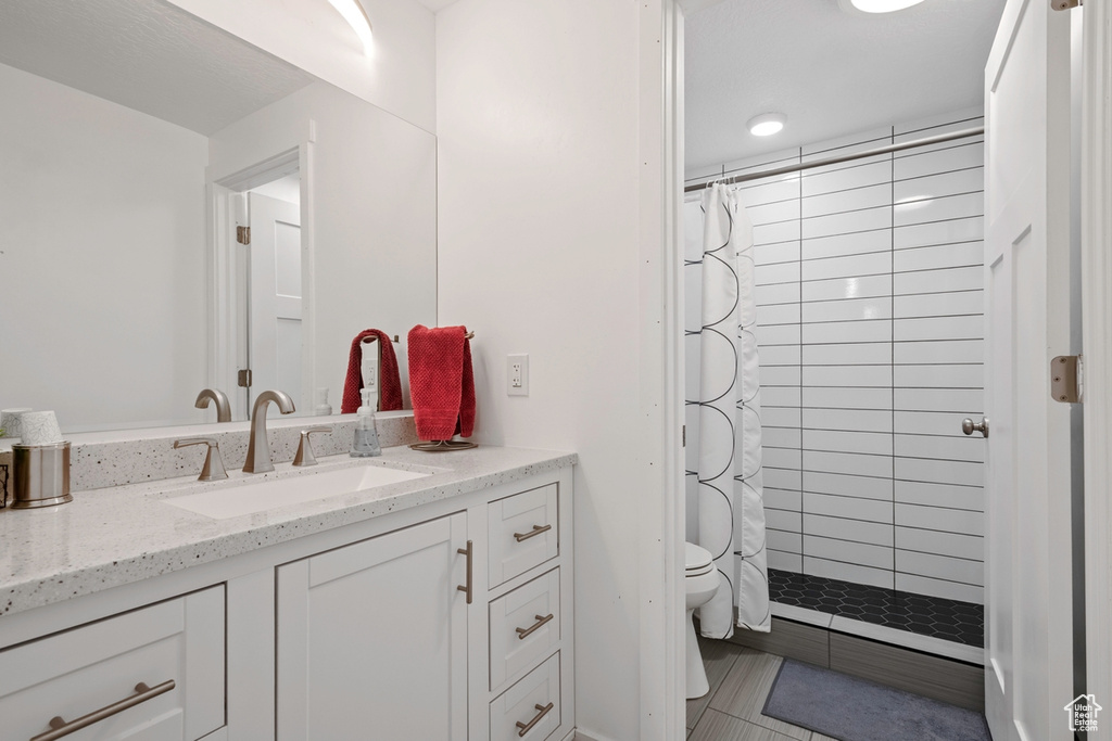 Bathroom featuring vanity, toilet, tiled shower, and tile patterned flooring