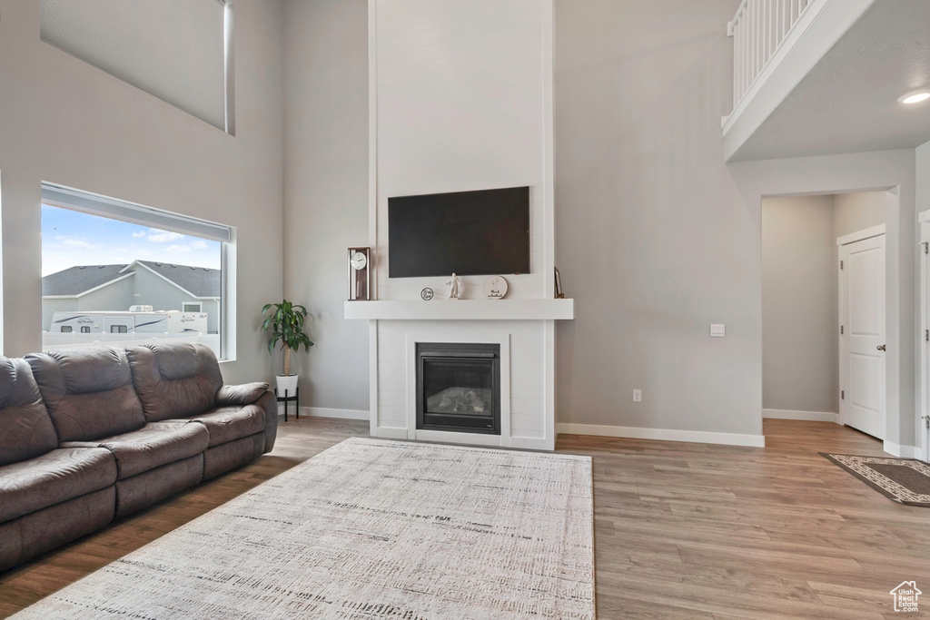 Living room with a high ceiling, light wood-type flooring, baseboards, and a glass covered fireplace
