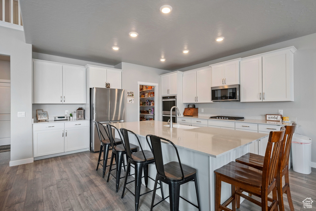 Kitchen with appliances with stainless steel finishes, a sink, dark wood-style floors, a kitchen bar, and a kitchen island with sink