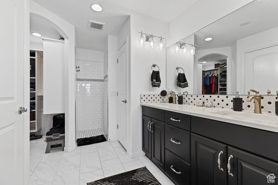 Bathroom with double vanity, a tile shower, a walk in closet, marble look tiles, and tasteful backsplash
