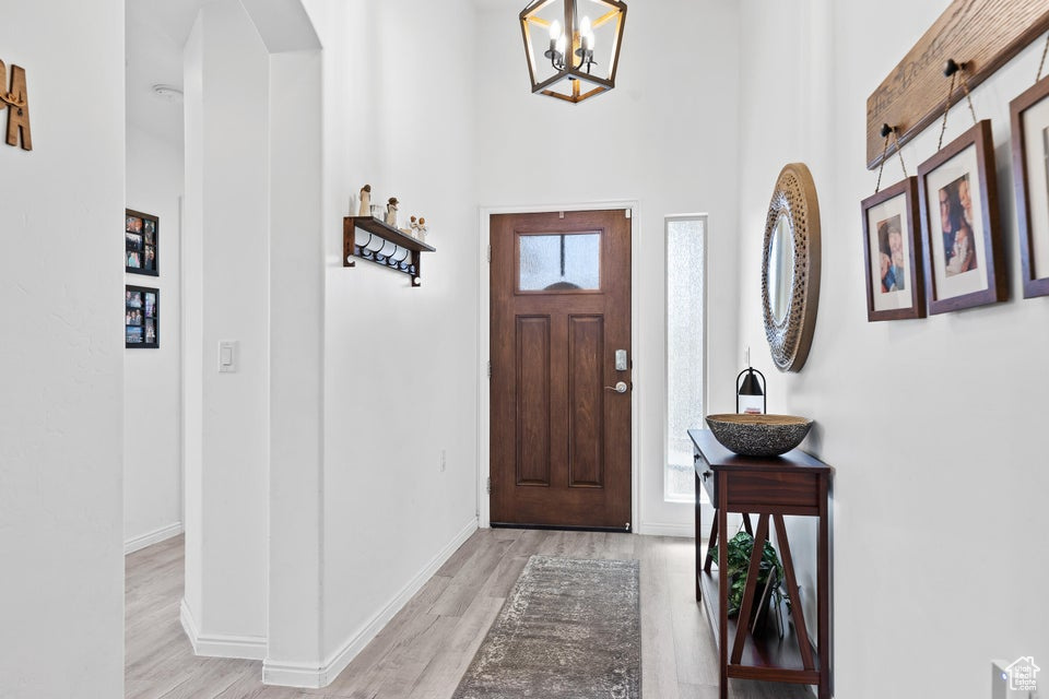 Foyer with arched walkways, light wood-type flooring, baseboards, a chandelier, and a towering ceiling