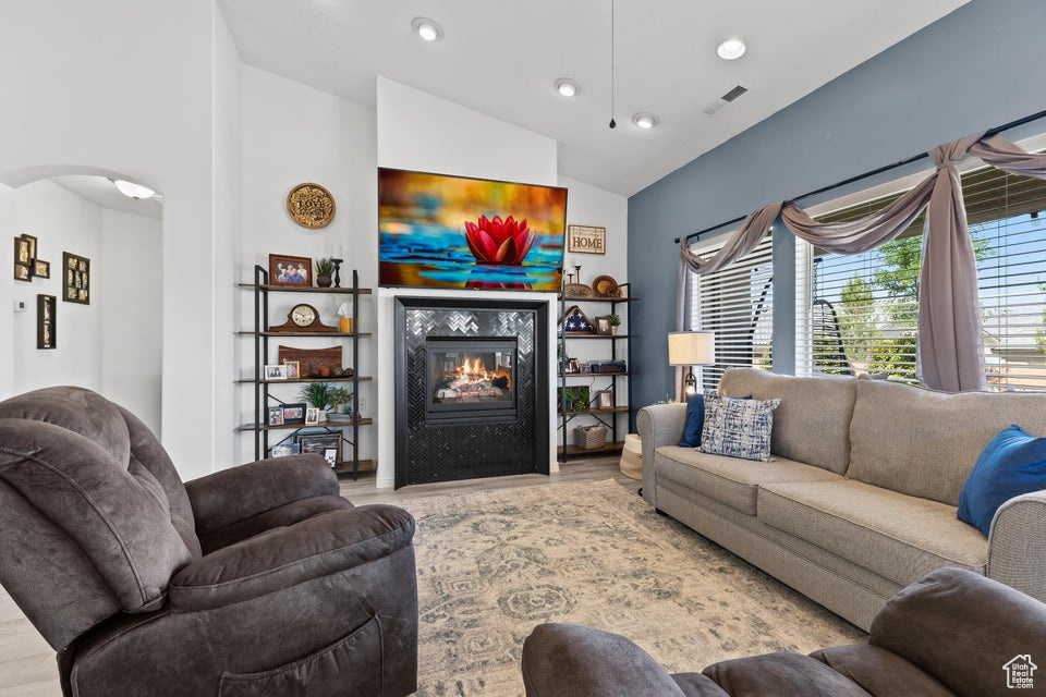 Living area featuring arched walkways, a glass covered fireplace, wood finished floors, recessed lighting, and lofted ceiling