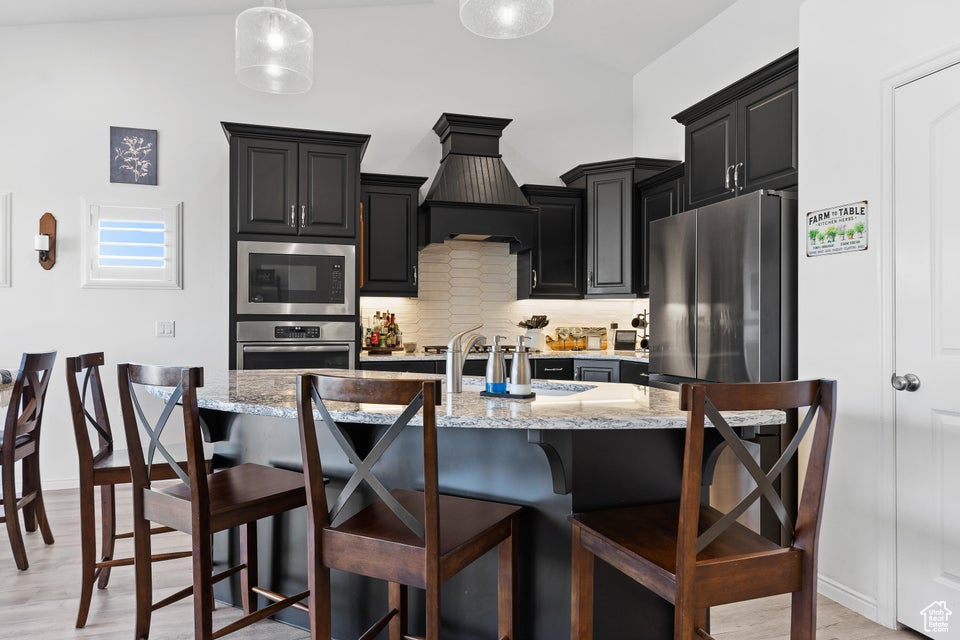 Kitchen featuring stainless steel oven, built in microwave, dark cabinets, custom range hood, and a breakfast bar area
