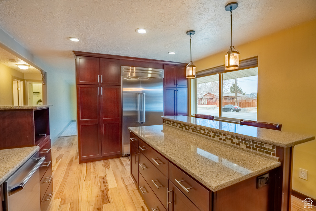 Kitchen with appliances with stainless steel finishes, light wood-style floors, a center island, a textured ceiling, and decorative light fixtures