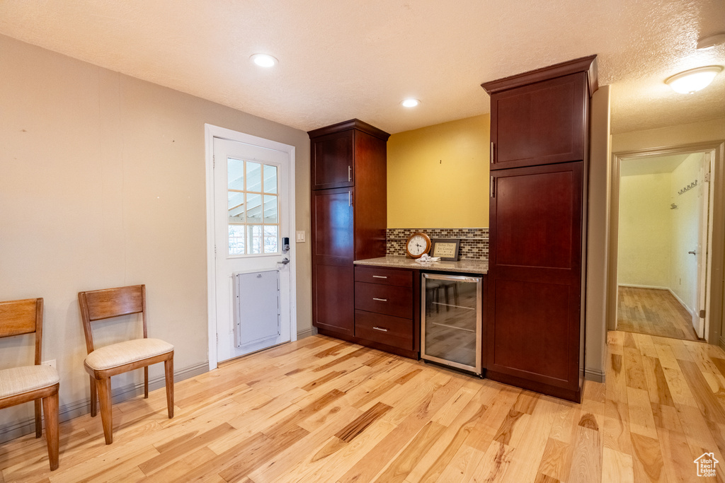 Indoor dry bar featuring beverage cooler, light wood-style floors, backsplash, baseboards, and recessed lighting