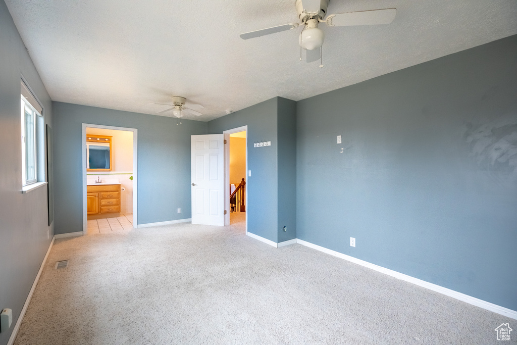 Unfurnished bedroom featuring baseboards, light carpet, a sink, ensuite bath, and a ceiling fan