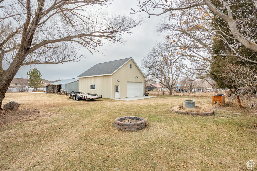View of home\\\'s exterior featuring an outdoor fire pit, an outdoor structure, a yard, and a detached garage