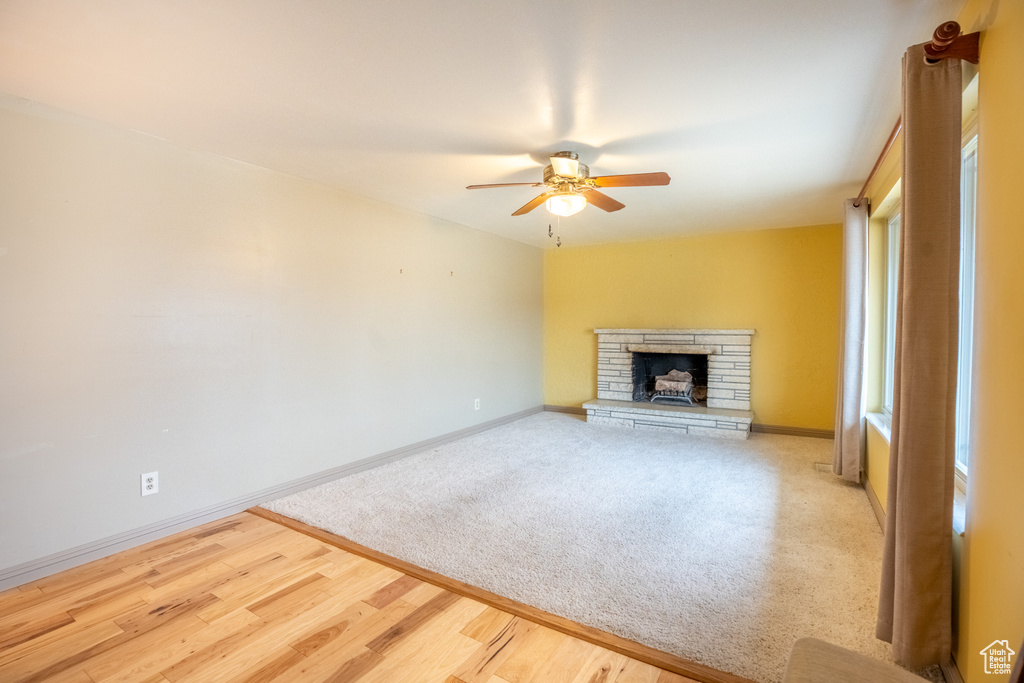 Unfurnished living room featuring ceiling fan, baseboards, a fireplace, wood finished floors, and carpet floors