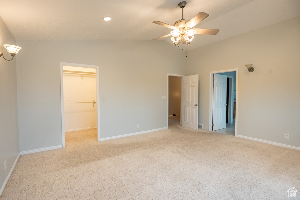 Unfurnished bedroom with light colored carpet, lofted ceiling, baseboards, a walk in closet, and ceiling fan