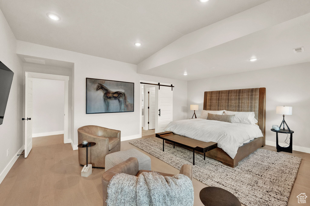 Bedroom with a barn door, baseboards, recessed lighting, wood finished floors, and vaulted ceiling