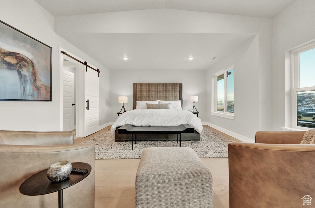 Bedroom featuring a barn door, multiple windows, vaulted ceiling, baseboards, and wood finished floors