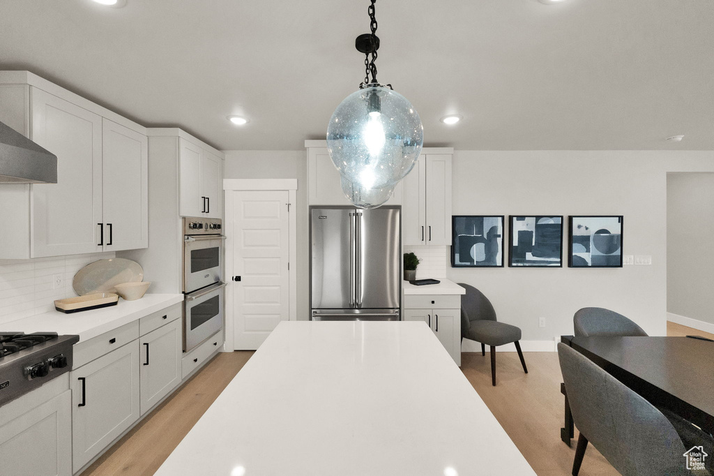Kitchen with appliances with stainless steel finishes, light wood finished floors, backsplash, light countertops, and recessed lighting