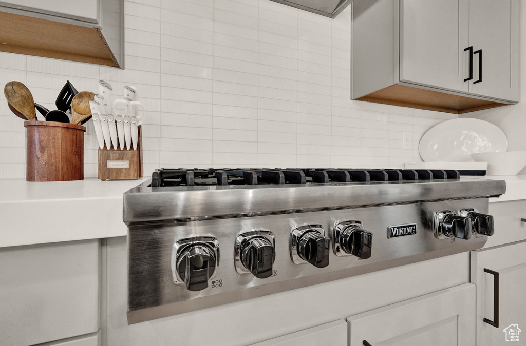 Kitchen view of decorative backsplash, stainless steel gas stovetop, and light countertops