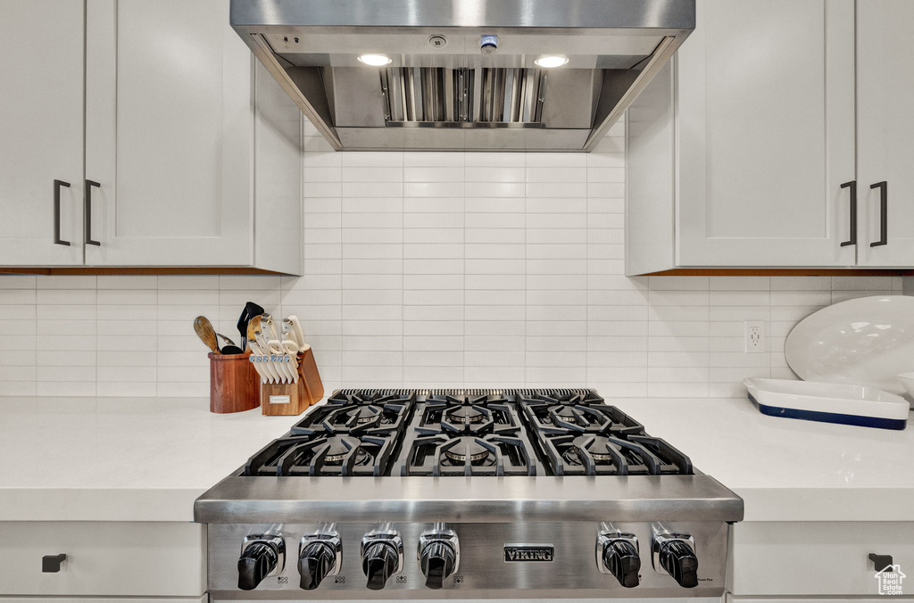 Kitchen featuring wall chimney range hood, light countertops, backsplash, and stainless steel gas stovetop