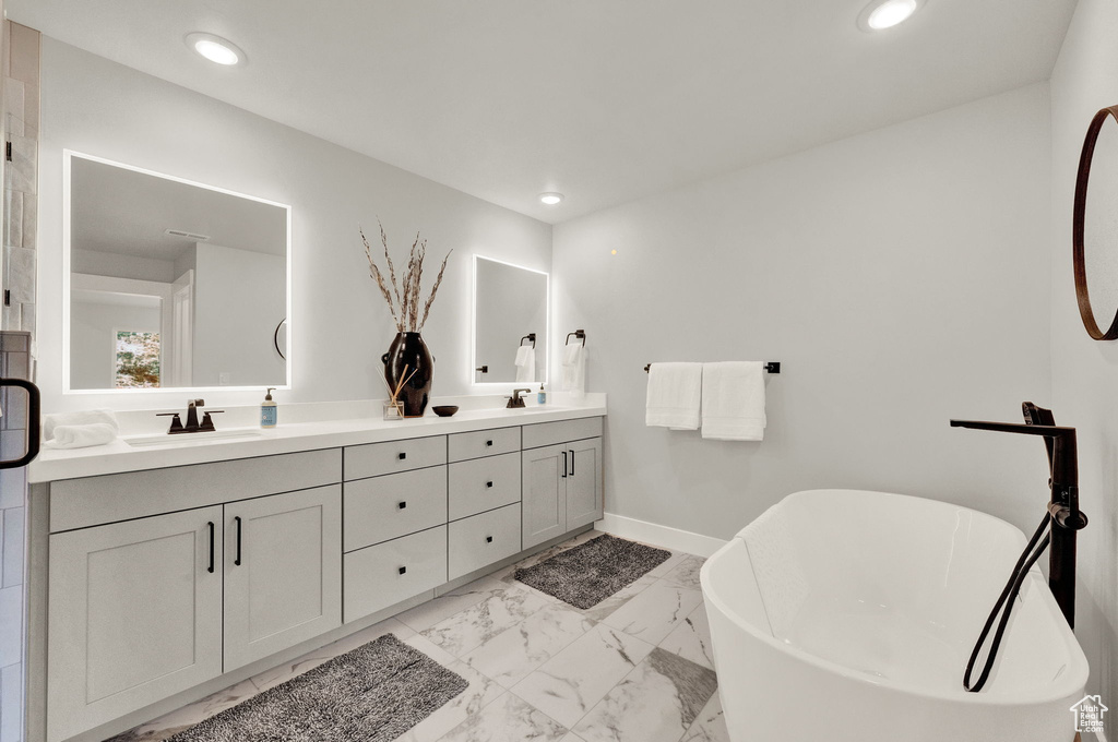 Full bath featuring double vanity, a soaking tub, marble look tiles, recessed lighting, and baseboards