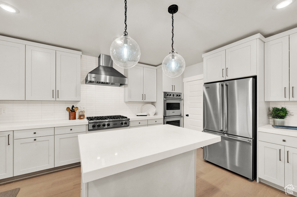 Kitchen featuring appliances with stainless steel finishes, wall chimney range hood, backsplash, light wood finished floors, and light countertops