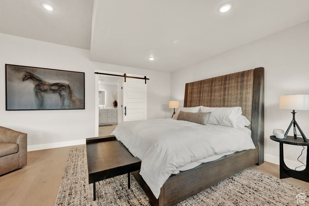 Bedroom featuring a barn door, baseboards, wood finished floors, recessed lighting, and ensuite bathroom