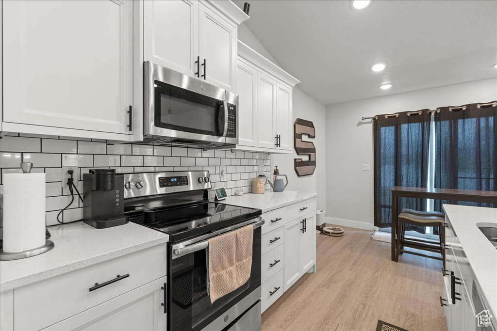 Kitchen with stainless steel appliances, backsplash, recessed lighting, white cabinets, and baseboards