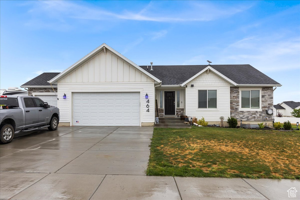 Single story home featuring an attached garage, a front lawn, concrete driveway, stone siding, and roof with shingles