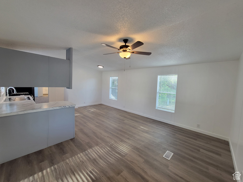 Unfurnished living room featuring a sink, dark wood-type flooring, ceiling fan, baseboards, and a textured ceiling