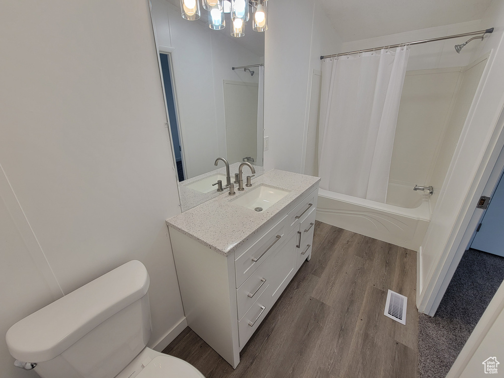 Full bathroom with wood finished floors, toilet, vanity, and shower / bath combo with shower curtain