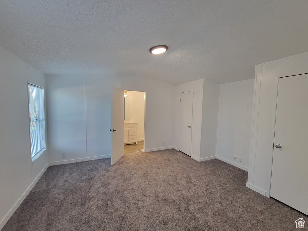 Unfurnished bedroom featuring carpet flooring, baseboards, ensuite bathroom, and a textured ceiling