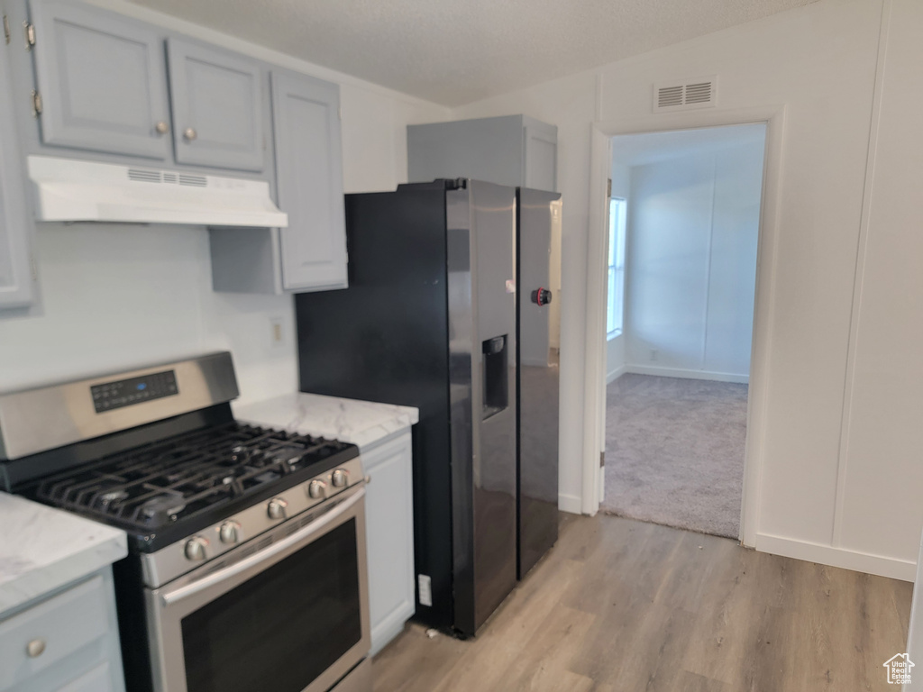 Kitchen featuring stainless steel appliances, under cabinet range hood, light wood finished floors, and light stone counters
