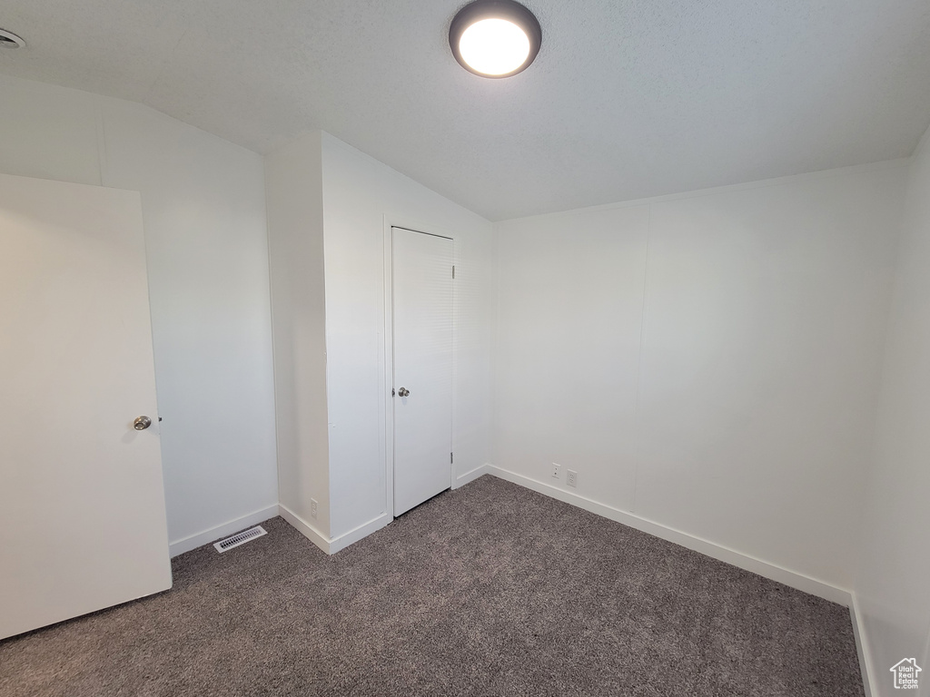 Unfurnished bedroom featuring dark colored carpet, baseboards, and vaulted ceiling