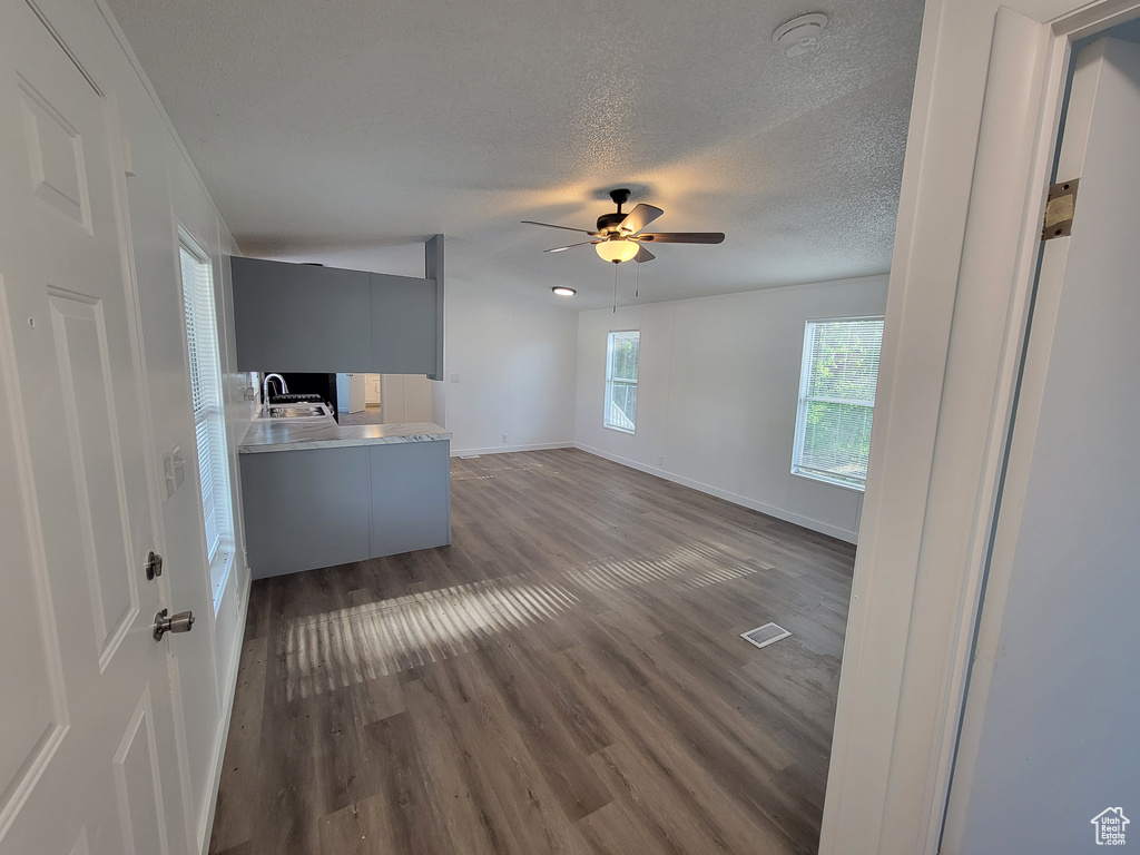 Unfurnished living room with a sink, dark wood-style floors, a textured ceiling, ceiling fan, and baseboards