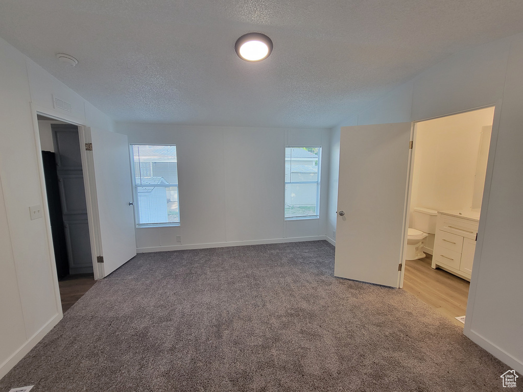Unfurnished bedroom featuring carpet flooring, a textured ceiling, baseboards, and ensuite bathroom