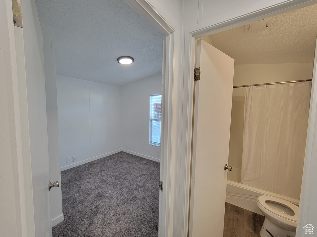 Bathroom with toilet, a textured ceiling, baseboards, and shower / bath combination with curtain