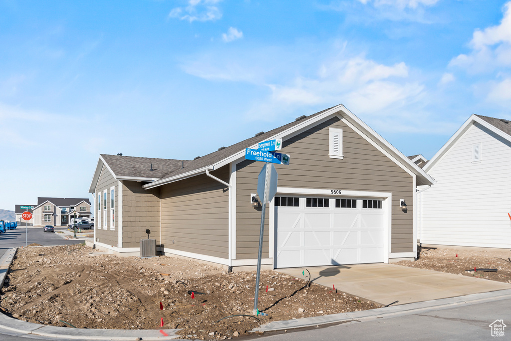 View of side of property with concrete driveway, an attached garage, and central AC unit