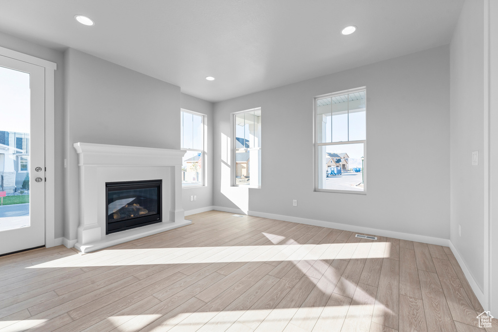 Unfurnished living room with light wood finished floors, plenty of natural light, a glass covered fireplace, baseboards, and recessed lighting