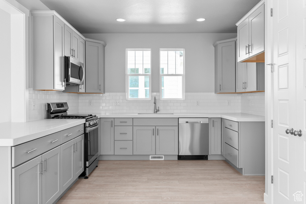 Kitchen with appliances with stainless steel finishes, a sink, gray cabinetry, and recessed lighting