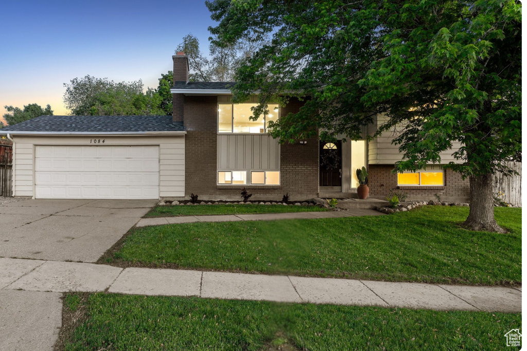 View of front of property featuring an attached garage, brick siding, a chimney, a front yard, and driveway
