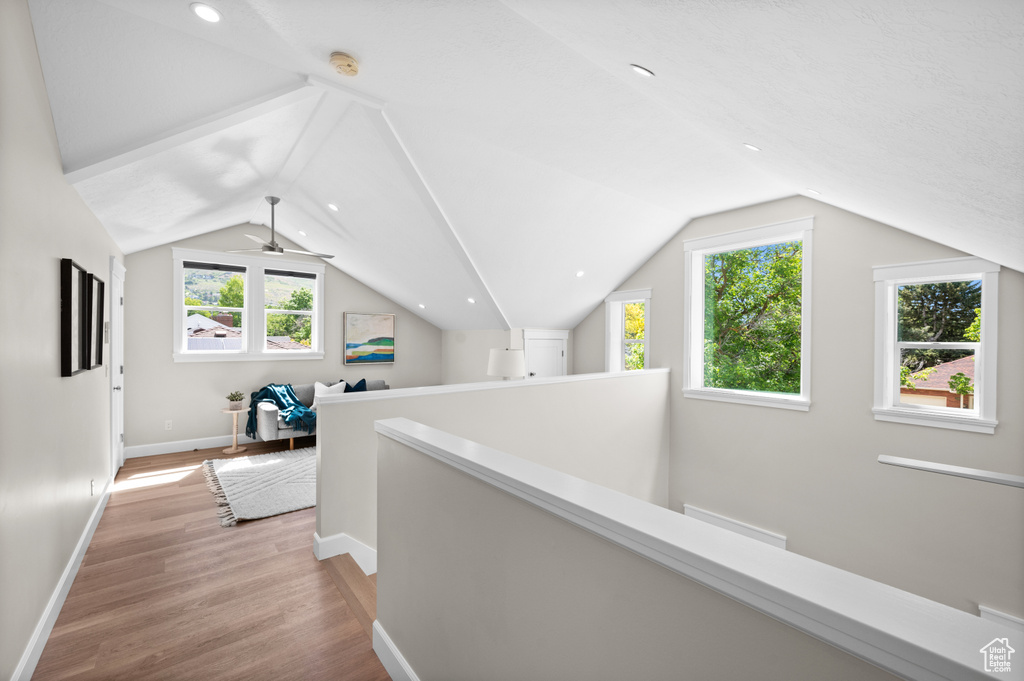 Hall with an upstairs landing, light wood finished floors, lofted ceiling, and baseboards