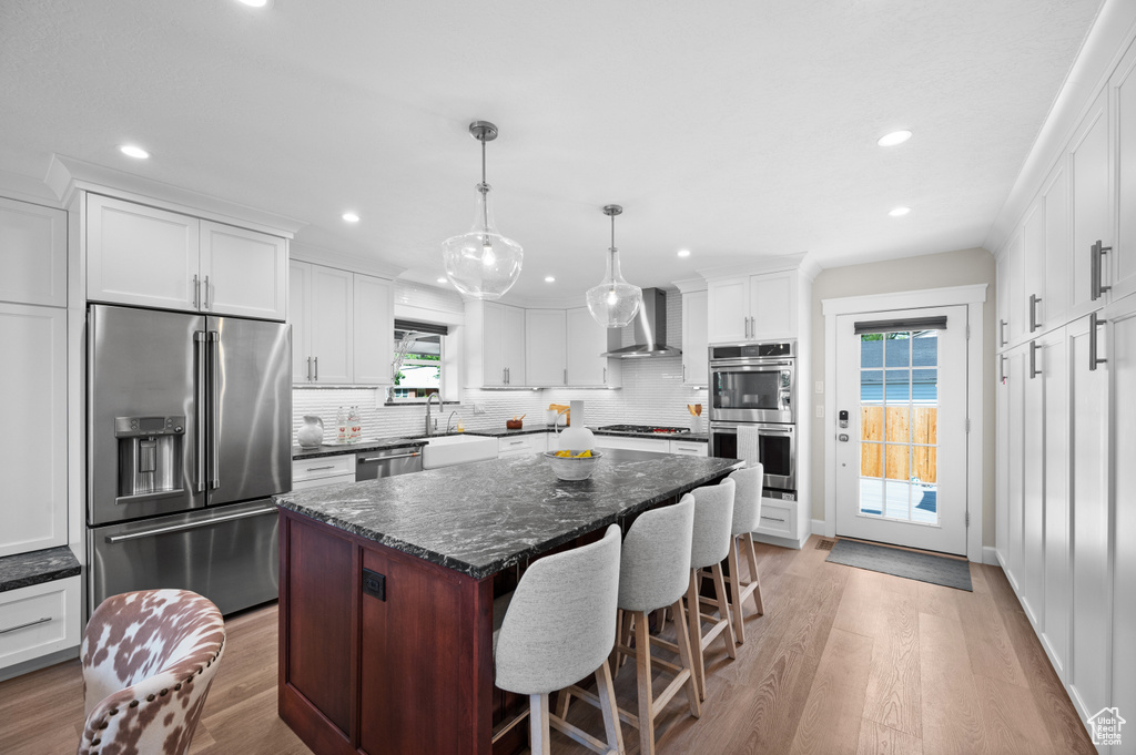 Kitchen featuring appliances with stainless steel finishes, wall chimney exhaust hood, light wood finished floors, tasteful backsplash, and recessed lighting
